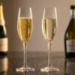Deux flûtes de vin pétillant, l'une de Champagne et l'autre de Prosecco, avec leurs bouteilles respectives.
